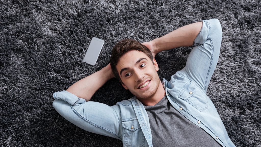 Southern Floor Company -portrait-of-a-smiling-casual-man-lying-on-the-carpet-with-mobile-phone-at-home